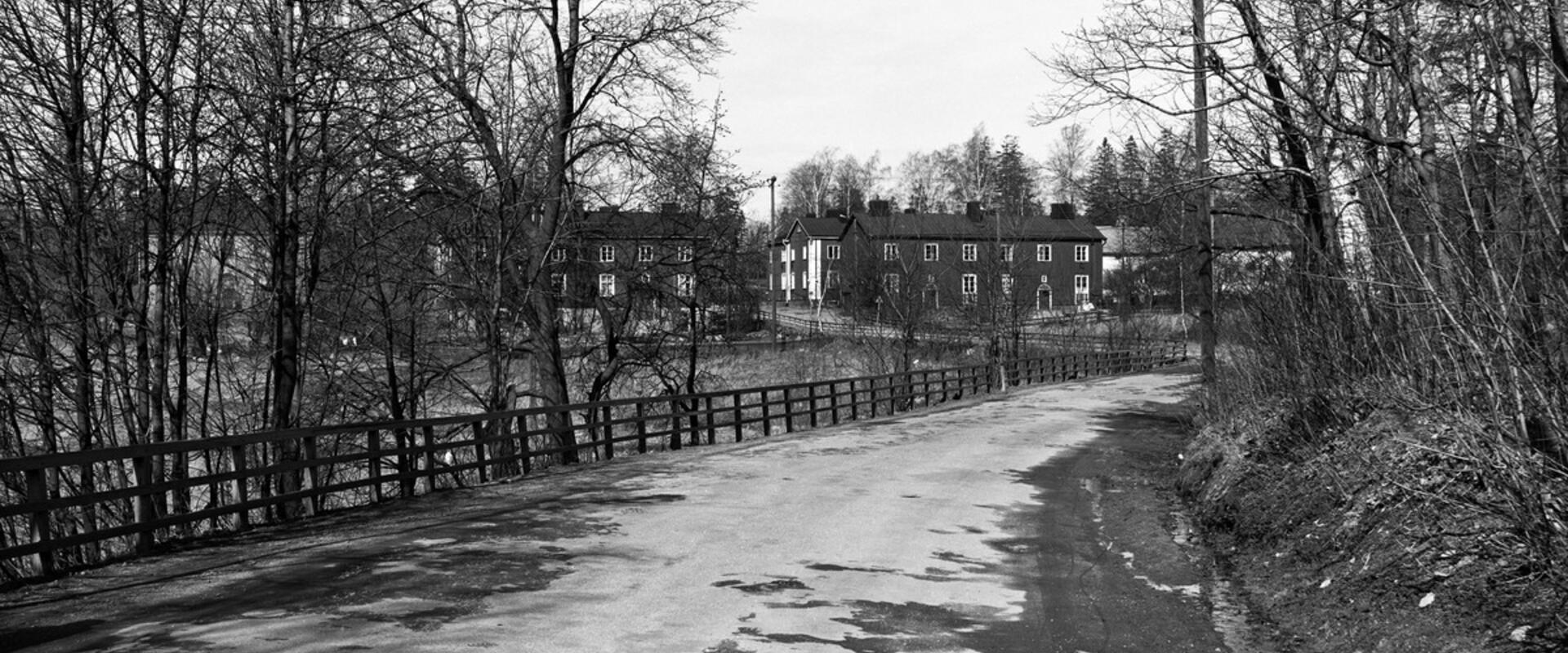 Maantie, jota reunustaa vasemmalla puukaide ja lehdettömät puut. Taustalla näkyy kaksikerroksisia puurakennuksia.