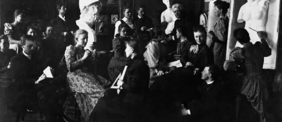 En grupp studerande har samlats i ett klassrum med målningar och skulpturer