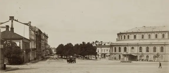 Vy från Skillnadsgatan norrut, mot Henriksesplanaden. I mitten av Skillnadstorget syns en omnibuss dragen av två hästar. Till höger Svenska teaterns byggnad som invigdes år 1866. Framför teatern står en brunn.