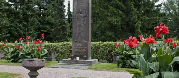 Harmaa kivipaasi pystyasennossa, johon kuvattu lippua heiluttava mies.