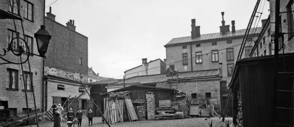 Aleksanterinkatu 52, sisäpiha. Sivuttain katsojaan seisoo nainen, jolla on lapsi sylissä. Kolme isompaa lasta seisoo rivissä keskellä pihaa. 