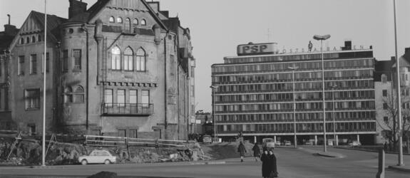 Rakennus purettiin pian kuvan ottamisen jälkeen, ja paikalle valmistui Ympyrätalo vuonna 1968. Kaksi ohikulkijaa on pysähtynyt katselemaan etualalla olevaa Kallion virastotalon rakennustyömaata. Oikealla näkyy Postisäästöpankin rakennus, Säästöpankinranta 2.