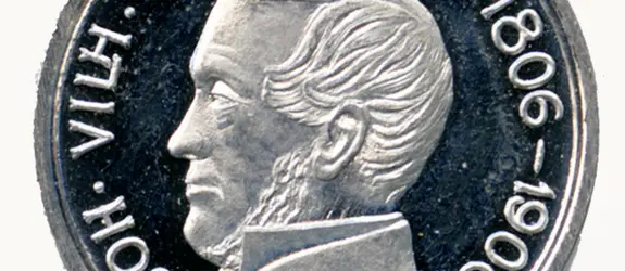 Keskellä hopeanväristä mitalia on miehen profiilikuva. Reunoja kiertää teksti JOH. VILH. SNELLMAN 1806–1906.