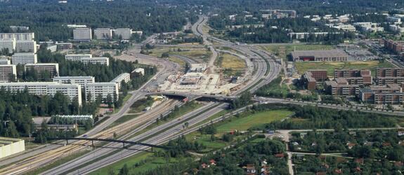 Flygbild över Östra centrums bygge längs med Österleden. Till höger av Österleden finns redan nya våningshus. På stället av metrostationen och köpcentret finns ännu ett bygge.