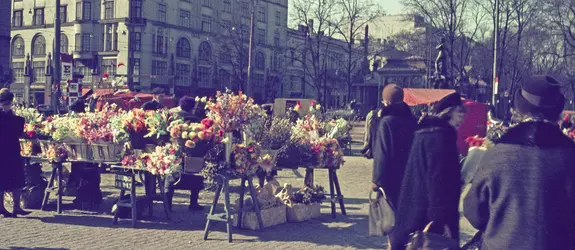 Färggranna blommor och påskprydnader på torget. Människor promenerar i förgrunden.