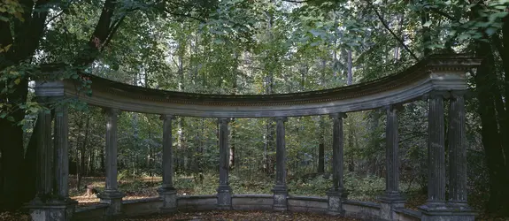 Harmaa pylväskaari metsän keskellä.