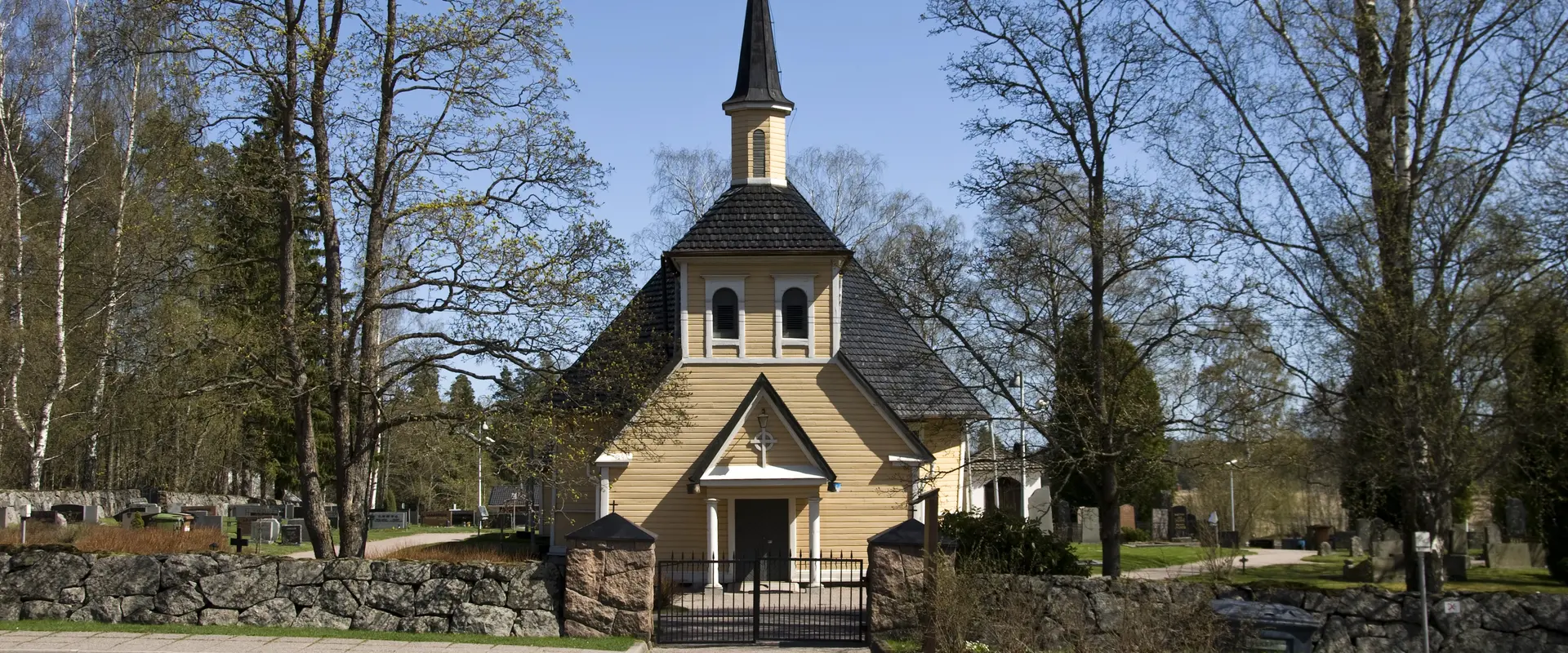 Kyrkobyggnad som omges av kyrkgård och en stenmur