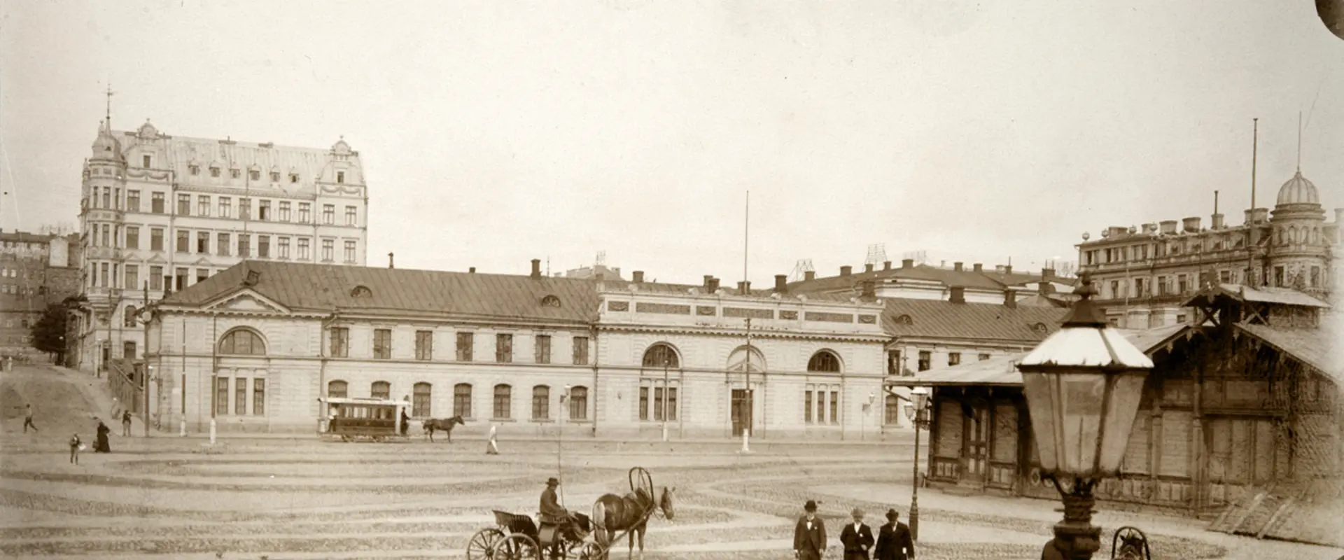Hyrvagnar med sina hästar och herrskap vid Södra hamnen på Packhustorget. I bakgrunden det tidigare arméförrådet, från 1888 packhuset, Västra Hamngatan 10 (nuvarande Södra kajen 10). På gatan en hästdragen spårvagn. Bakom förrådet syns ett femvåningshus från 1960-talet vid hörnet av Unionsgatan 14 – Södra Magasinsgatan 3.