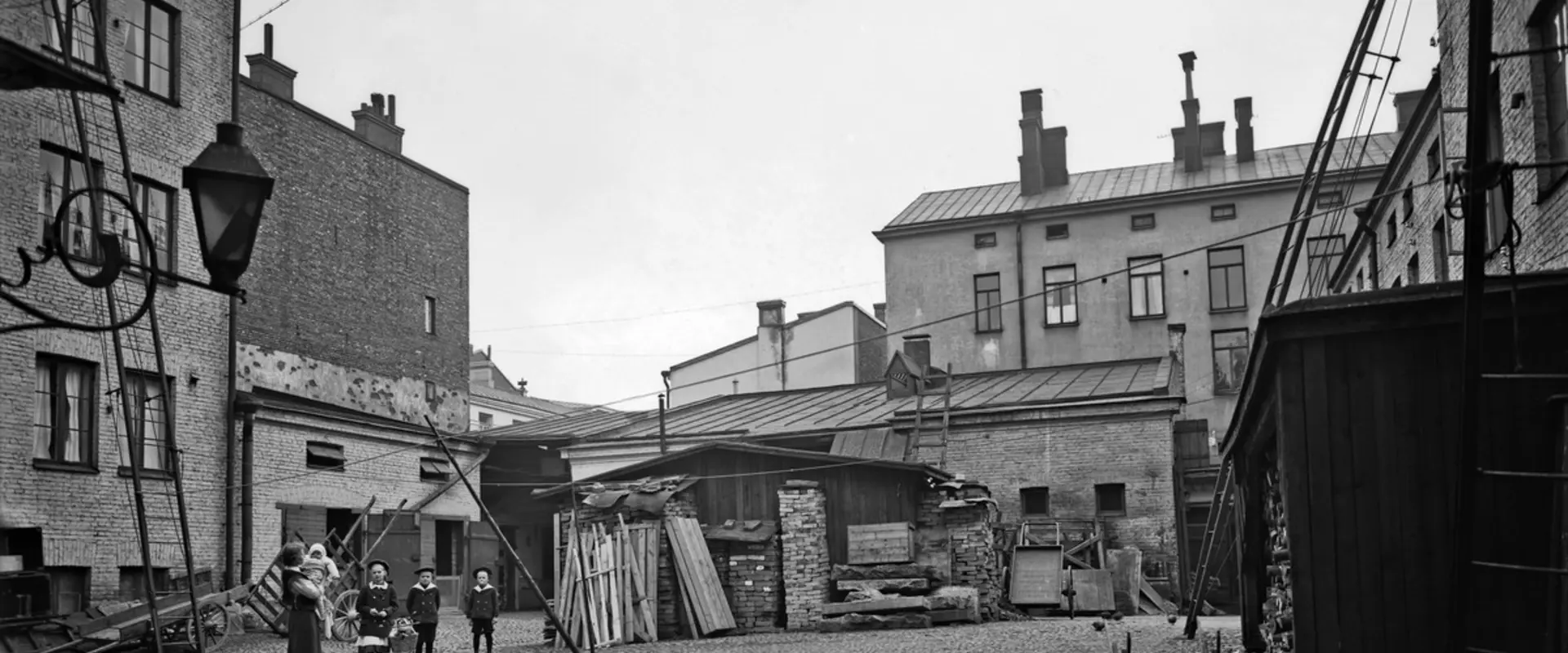 Aleksanterinkatu 52, sisäpiha. Sivuttain katsojaan seisoo nainen, jolla on lapsi sylissä. Kolme isompaa lasta seisoo rivissä keskellä pihaa. 
