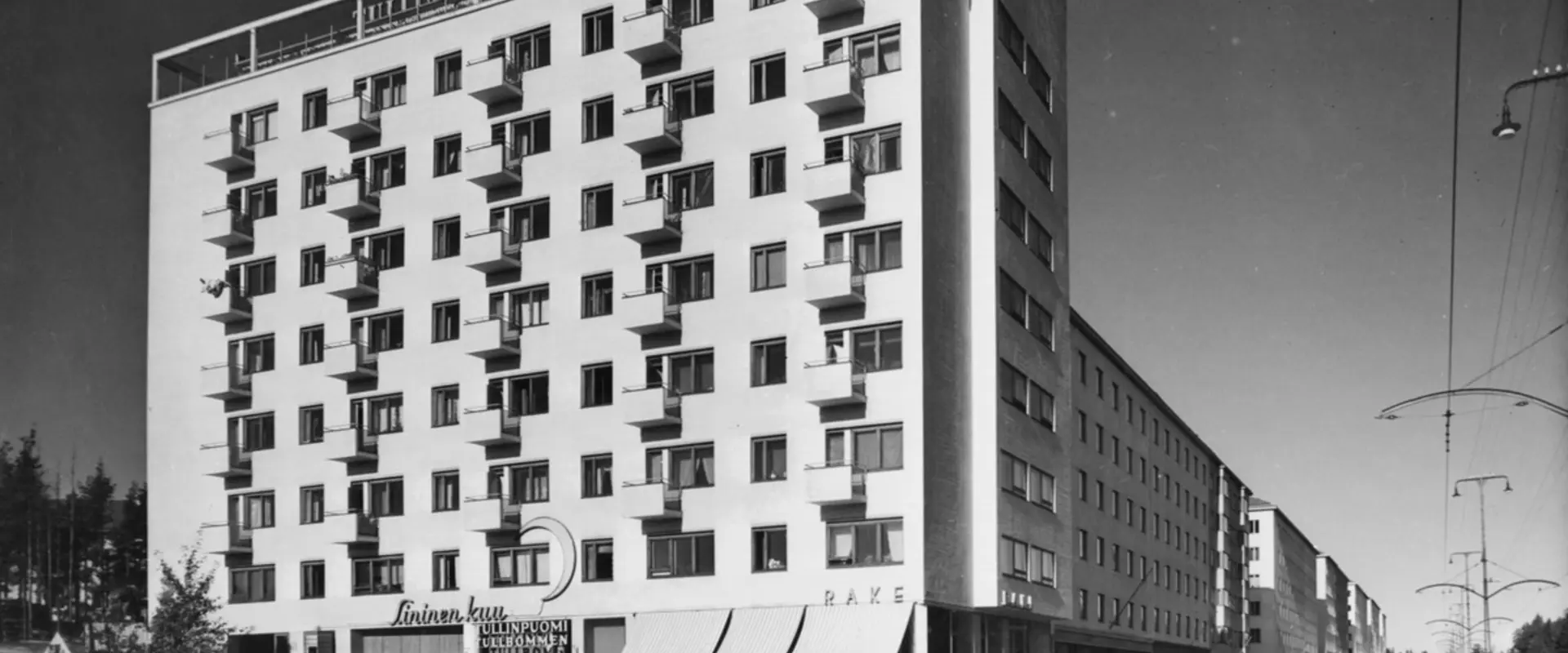 Åbovägen 90 (= Mannerheimvägen 118). Tullbommens byggnad. Arkitekt Olli Pöyry, färdig 1940. En ljus åtta våningars byggnad vars övre del bär neonbokstäverna Tullinpuomi Tullbommen och högra kanten KINO.