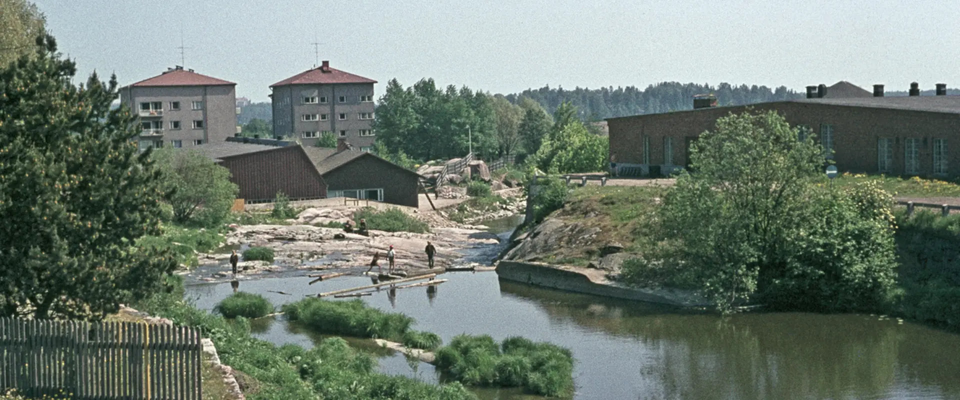 Lapset ovat leikkimässä Vanhankaupunginkoskella. Oikealla on Kuninkaankartanonsaari. Taustalla olevat kerrostalot Katariina Saksilaisen katu 11 - Pornaistenniemenpolku 2.