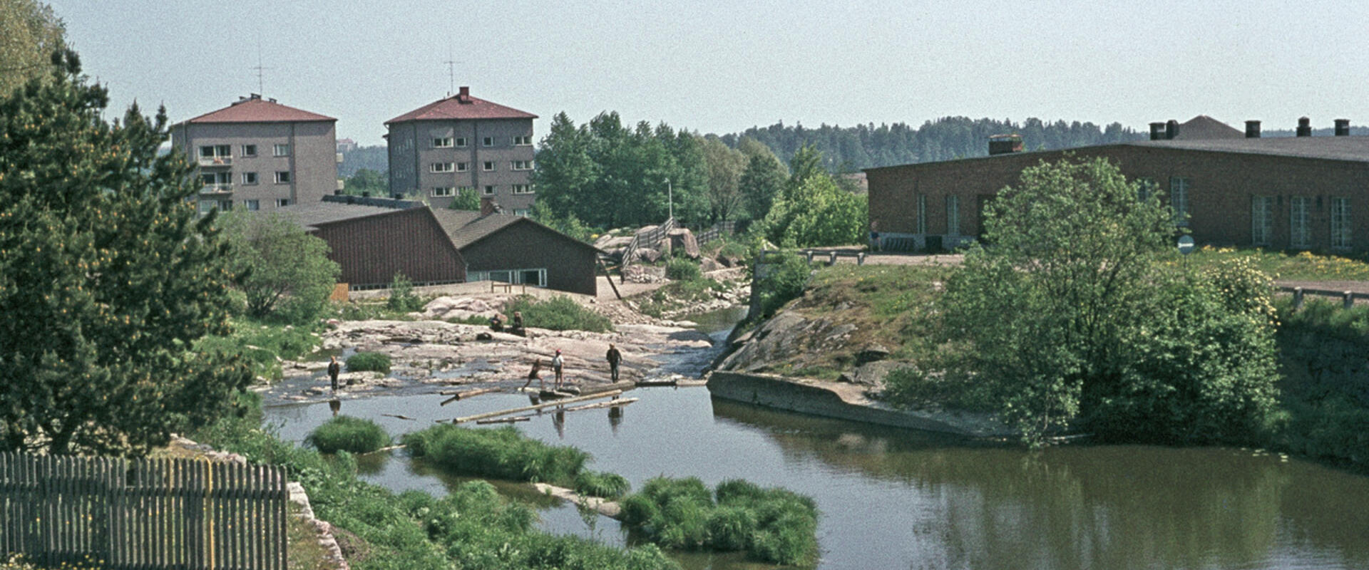 Lapset ovat leikkimässä Vanhankaupunginkoskella. Oikealla on Kuninkaankartanonsaari. Taustalla olevat kerrostalot Katariina Saksilaisen katu 11 - Pornaistenniemenpolku 2.