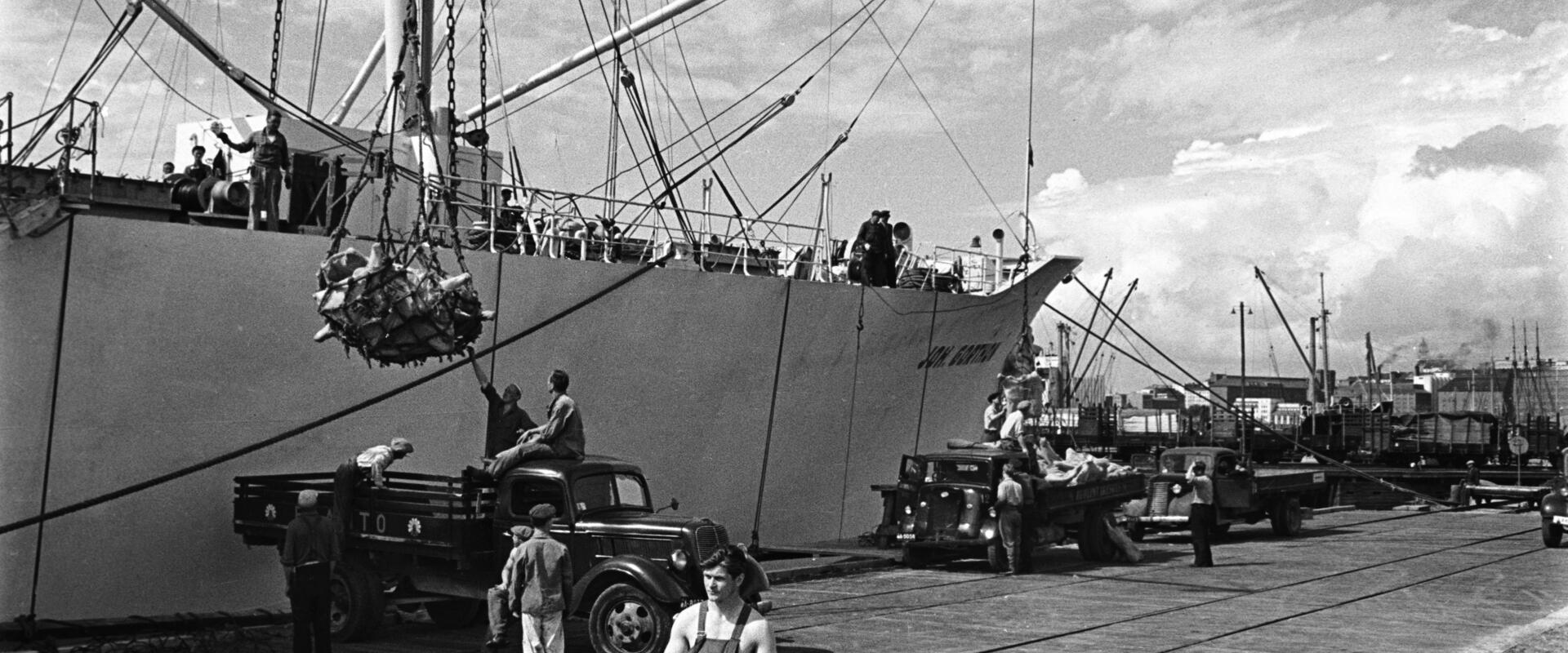Lasten av ett handelsfartyg håller på att lossas med vinscher till lastbilsflak i Sörnäs hamn.
