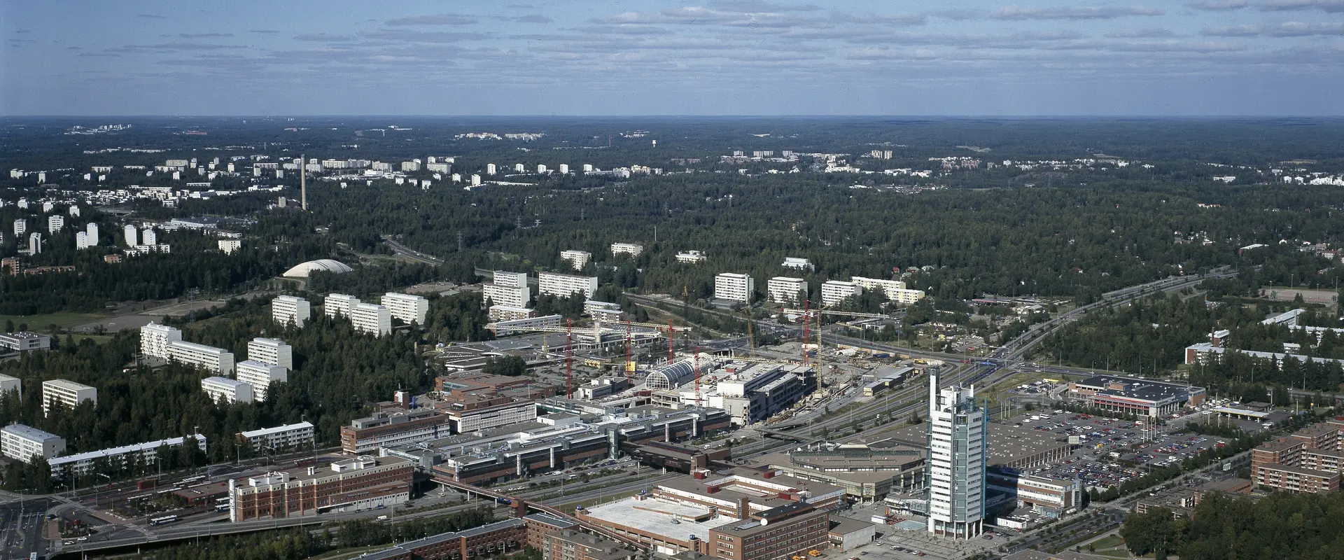 Flygbild över stadsdelen Östra centrum från söder mot norr. I förgrunden Österleden och nya byggnader, i bakgrunden skog och äldre höghus.