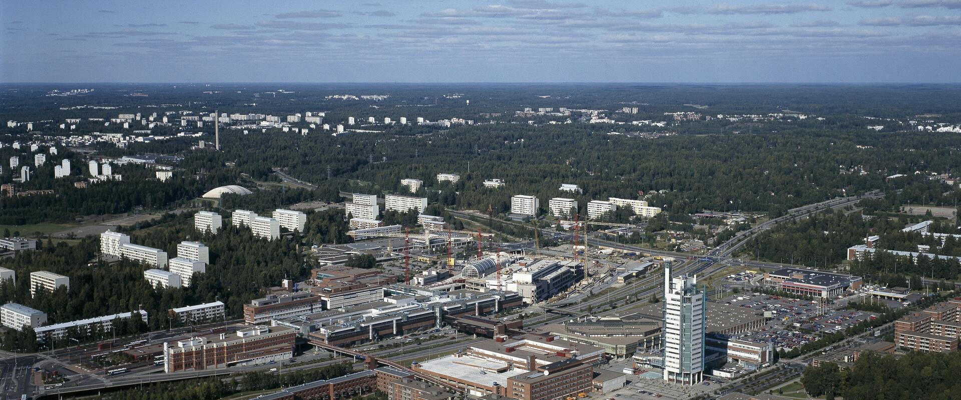 Flygbild över stadsdelen Östra centrum från söder mot norr. I förgrunden Österleden och nya byggnader, i bakgrunden skog och äldre höghus.