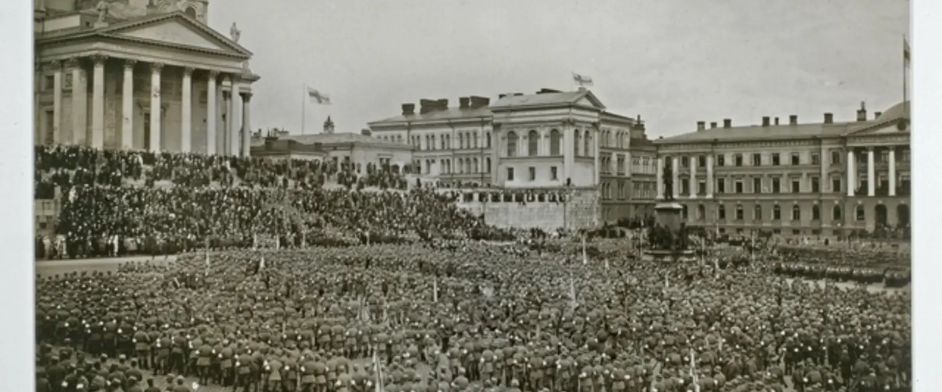 Massor av soldater som står i rader. Gruppen fyller nästan hela Senatstorget. I bakgrunden syns Domkyrkan och Statsrådsborgen.