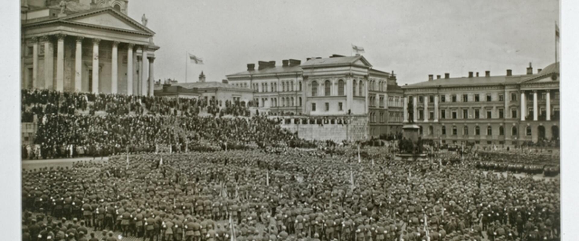 Massor av soldater som står i rader. Gruppen fyller nästan hela Senatstorget. I bakgrunden syns Domkyrkan och Statsrådsborgen.