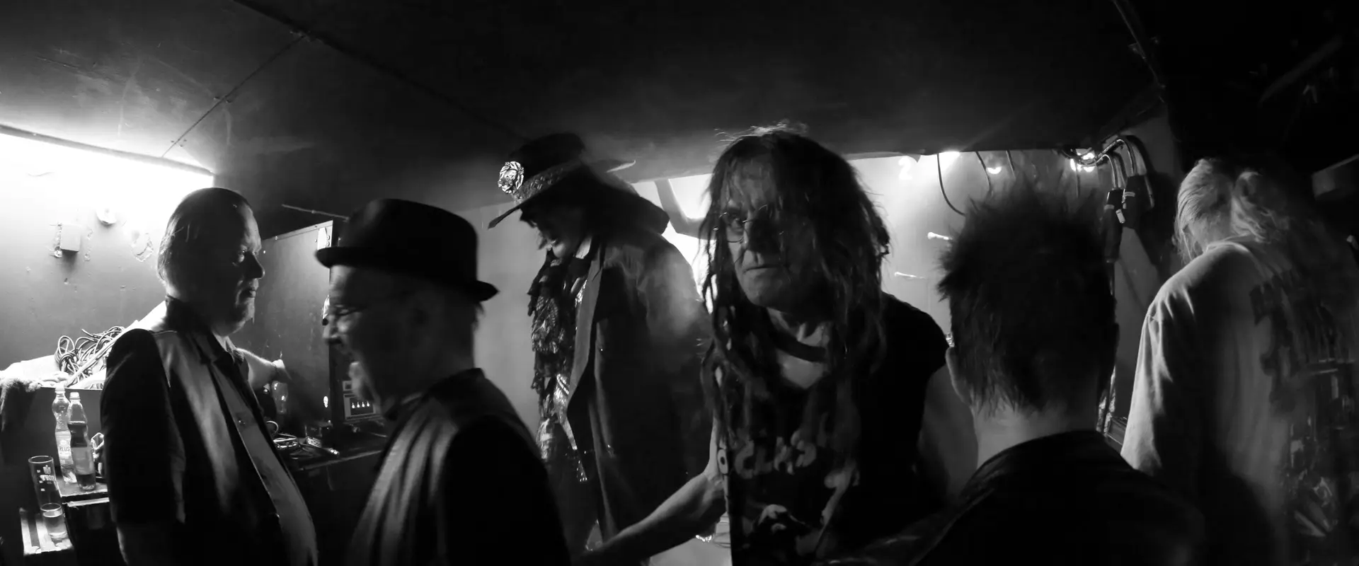Rockmusiker i en dunkel bar. Mitt på bilden står Pelle Miljoona och tittar in i kameran. Bakom honom står Andy McCoy.