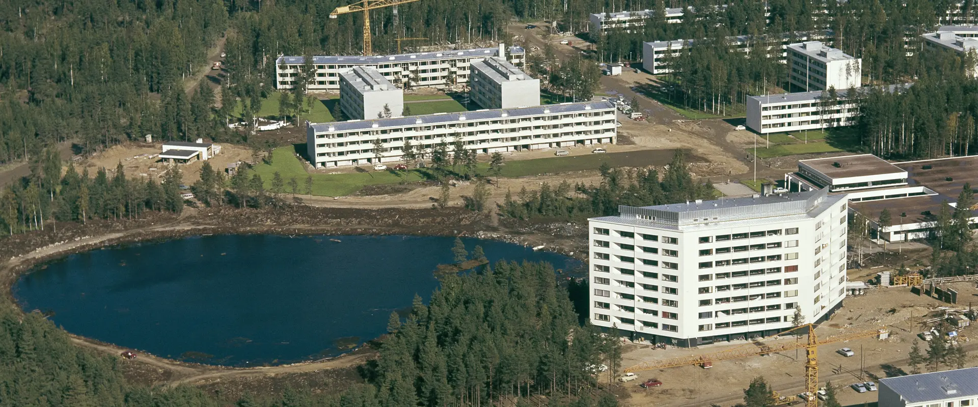 Flygbild av en damm med vita våningshus vid stranden.