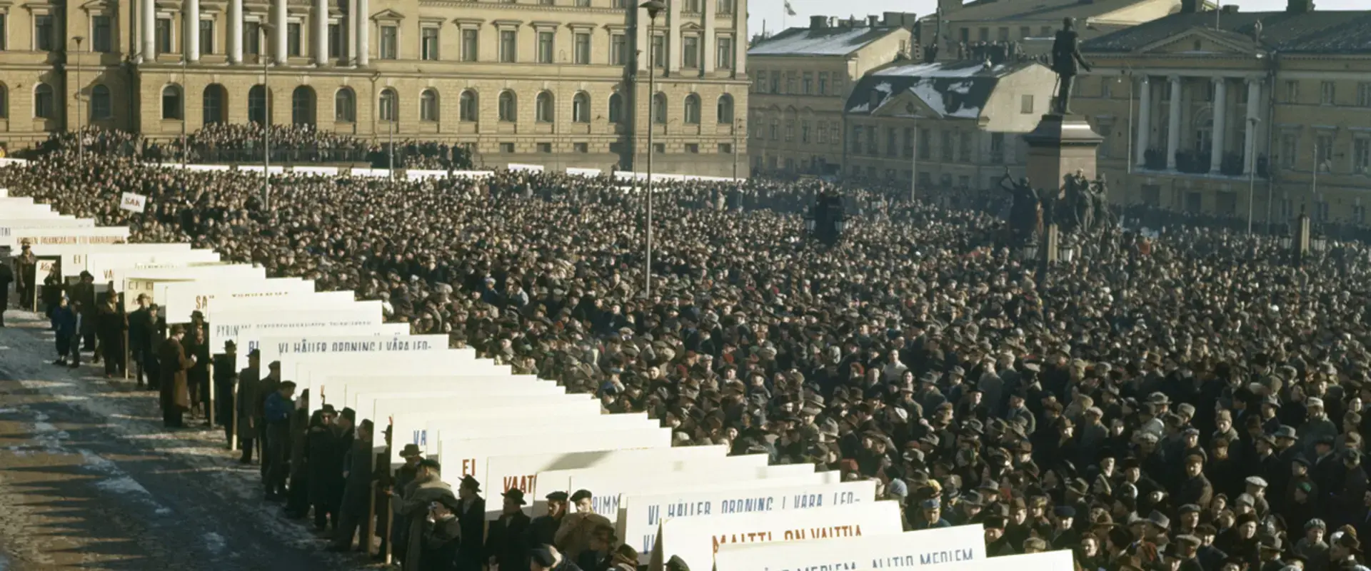 Mielenosoitus yleislakon aikaan Senaatintorilla maaliskuussa 1956. Edustalla SAK:n kylttejä, taustalla Valtioneuvoston linna, Sederholmin talo ja Bockin talo.