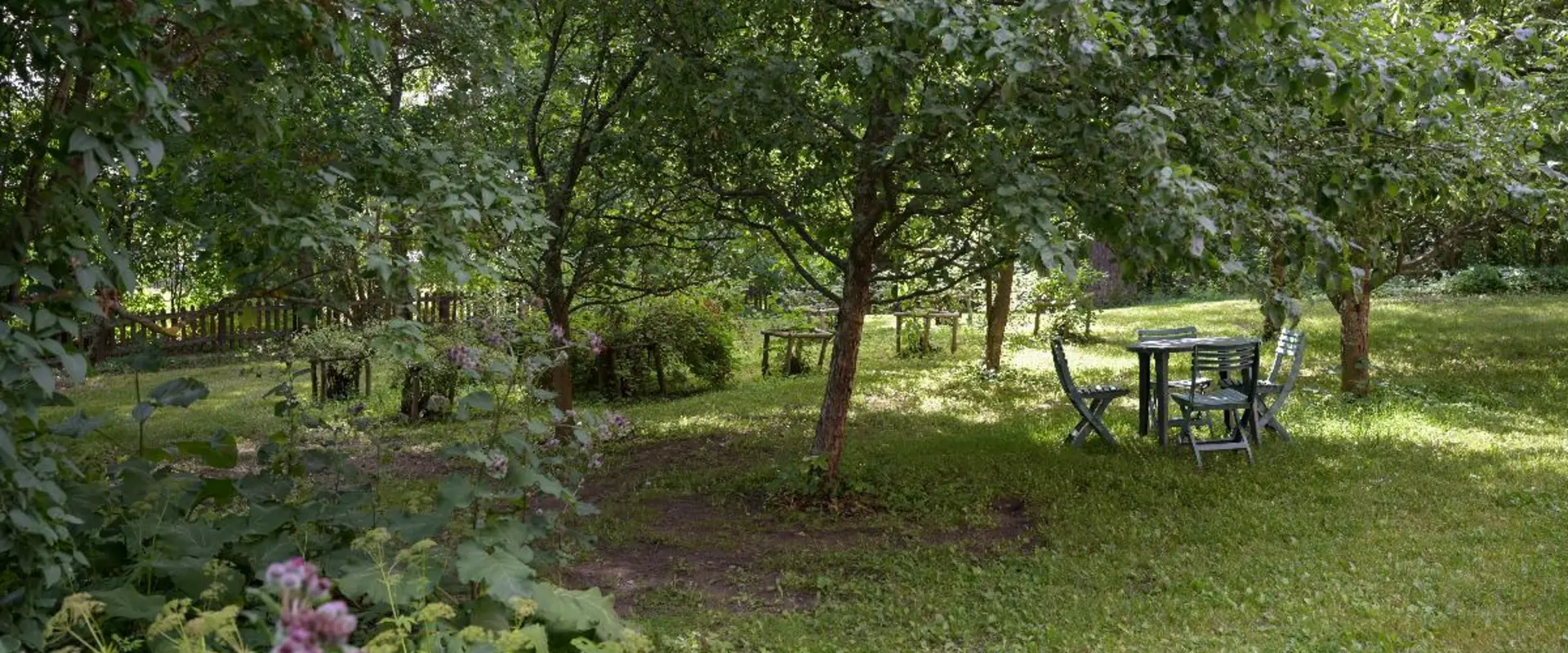Nurmikkoa, puita ja pensaita, keskellä on pieni pöytä, jonka ympärillä on neljä tuolia.