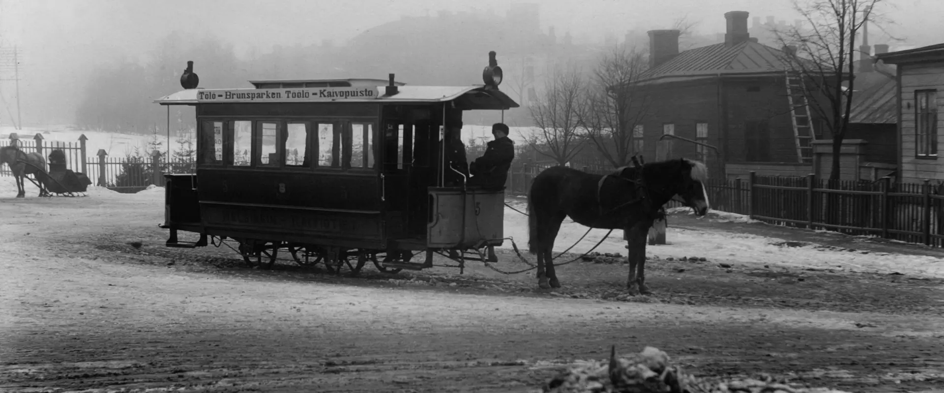 Hästspårvagn på vintern. I bakgrunden hus i dimma.