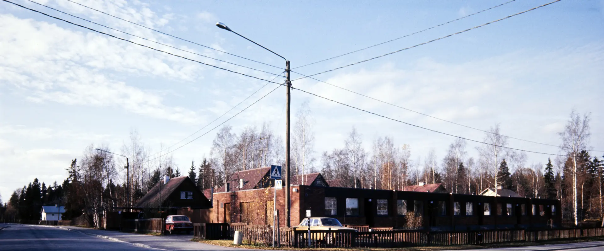 Radhus i rödtegel med plant tak, bakom dem syns egnahemshus med sadeltak.