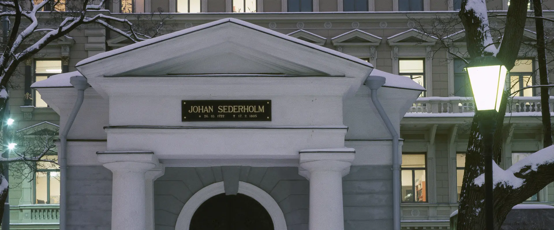 Foto av en liten stenbyggnad, dekorerad i nyklassisk stil. Ovanför dörren står det Johan Sederholm.