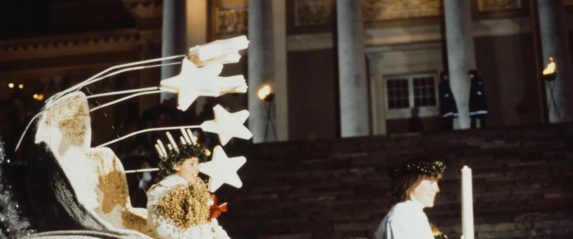 Lucia sitter i en vagn med stjärndekorationer framför Domkyrkan.