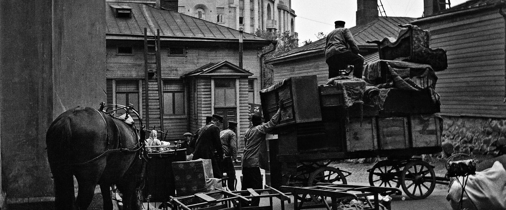 Ihmisiä muuttopuuhissa Läntinen Heikinkatu 24:n (Mannerheimintie 18:n kohdalla). Ihmiset lastaavat sisäpihalla laatikoita hevoskärryjen selkään.
