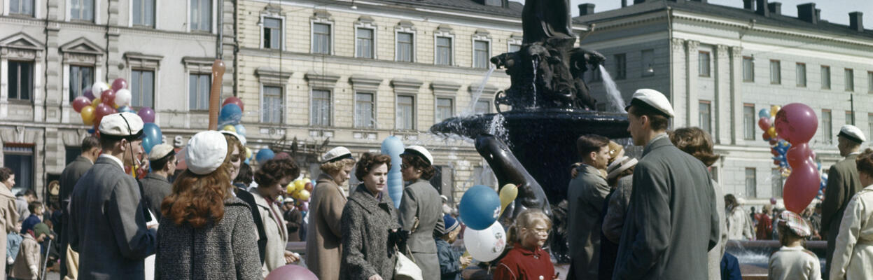 Aikuisia ja lapsia kokoontuneena Havis Amandan ympärille. Joillakin on ylioppilaslakki, joillakin kädessään ilmapallo.