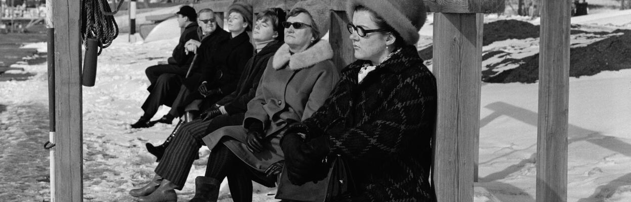 naisia istuu natonkuivaustelineen alustalla talvivaatteissaan. Vasemmalla pelastusrengas.