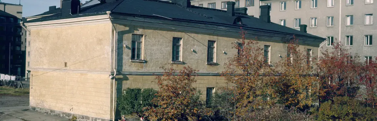 Kaksikerroksinen keltainen kivirakennus, jossa on musta aumakatto ja kahdeksanruutuiset ikkunat.