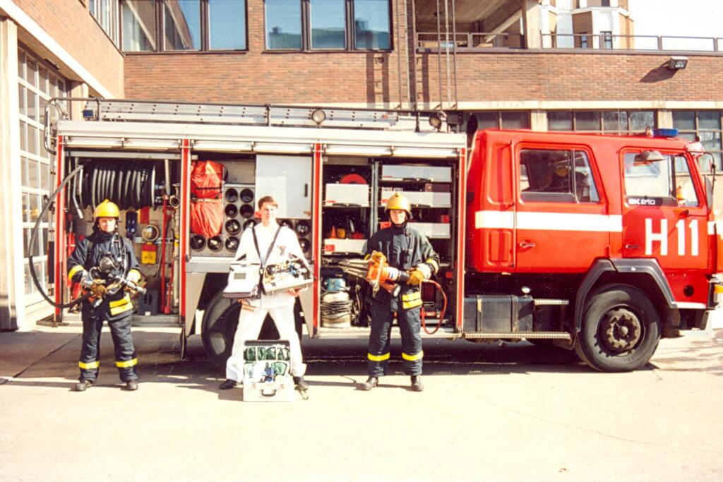 Vuonna 1991 hankittiin Sisu Sk210 -pelastusauto, joka otettiin mukaan ensihoitojärjestelmään ensivasteyksikön rooliin.
Kuvassa kalusto ja miehistö havainnollistavat yksikössä työskentelevien pelastajien rooleja sekä sammutus-, lääkintä- ja pelastusvalmiutta. Ensivasteyksikön kokonaismiehitys on esimies ja viisi pelastajaa.  Kuvaaja: Pelastusmuseo