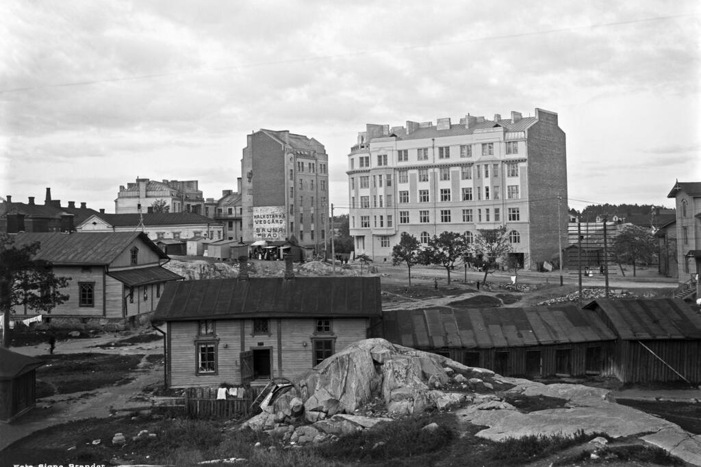 Kivitalon seinässä mainostetaan halkotarhaa ja saunaa, jotka kumpikin olivat tärkeitä palveluja 1900-luvun alkupuolella. Työläiskaupunginosan uusien kivitalojen pienissä asunnoissa ei yleensä ollut kylpyhuonetta, ja huoneissa oli kaakeliuunit. Kuvaaja: Helsingin kaupunginmuseo / Signe Brander