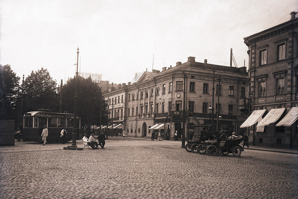 Helsingfors första taxistation låg vid kanten av Salutorget. Framför stationen stod en Oldsmobile och bredvid en delvis täckt Cadillac, båda från 1905. Det första taxilovet utfärdades 1906. Foto: Helsingfors stadsmuseum / Harald Rosenberg