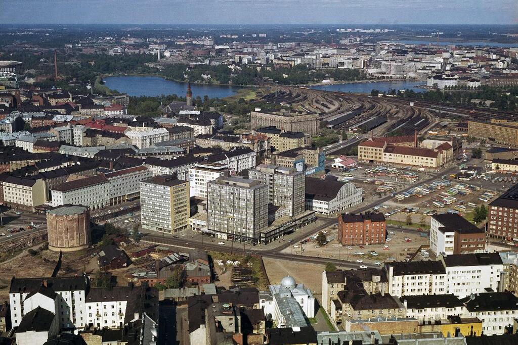 Kampen, i mitten Bilhuset och Tennispalatset. Till vänster Kampens gasklocka som byggdes 1907, och revs 1968. Framför Bilhuset en kasern som revs ungefär samtidigt. Parkeringsplatsen för bussar är i dag Kampens centrum. Bakom fältet ligger Jordbrukarnas mjölkcentrals byggnad. Foto: Helsingfors stadsmuseum / Sky-Foto Möller