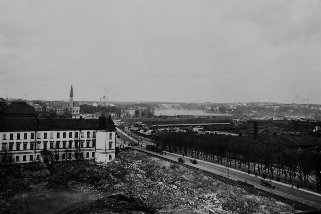 Västra Henriksgatan 28 (nuvarande Mannerheimvägen 22–24), ruinerna av Åbo kasern, till höger gasverket, bakom det bangården. I bakgrunden syns Nationalmuseet och Tölöviken.  Foto: Helsingfors stadsmuseum