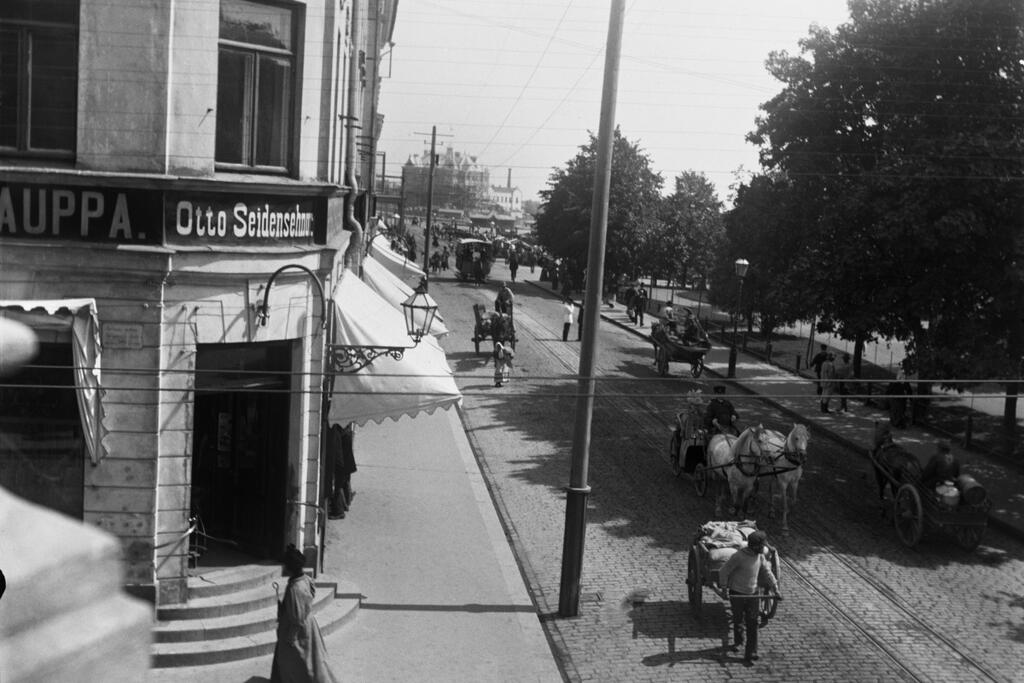 Trafik på Norra Esplanaden på 1890-talet. I vänstra hörnet syns Otto Seidenschnurs butik för ”Nordiska hushållsartiklar”. Foto: Helsingfors stadsmuseum / Ester Heikel