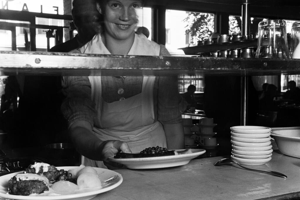 Elannon kansanravintolassa annokset tilattiin ja maksettiin tiskillä, tarjoilija toi ne pöytiin. Tarjolla oli kotiruokaa ja ruokajuomaksi maitoa. Kuvaaja: Helsingin kaupunginmuseo