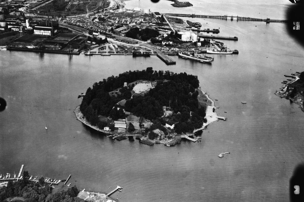 På Sumparn fanns en trädgård, ett utsiktstorn och trävillor som beboddes permanent av ett trettiotal personer i början av 1900-talet. Det var ett populärt rekreationsområde dit man kunde ta sig med ångbåt eller fast roddbåt. Holmen överläts på 1920-talet till andelsaffären Elanto som upprätthöll en sommarkoloni för sina anställdas barn från 1920-talet till 1976. Sumparn förenades med Sörnäs hamn genom sprängning och markutfyllnad under åren 1958–62. Foto: Helsingfors stadsmuseum / Flygvapnet