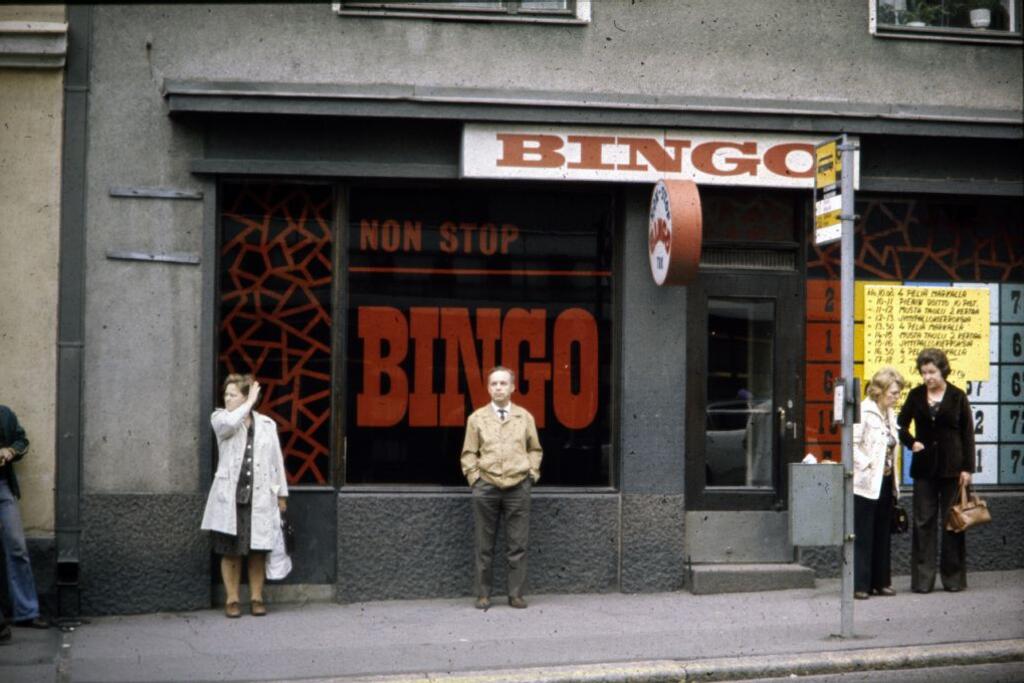 ihmisiä seisoo non stop bingo -liikkeen edessä bussipysäkillä