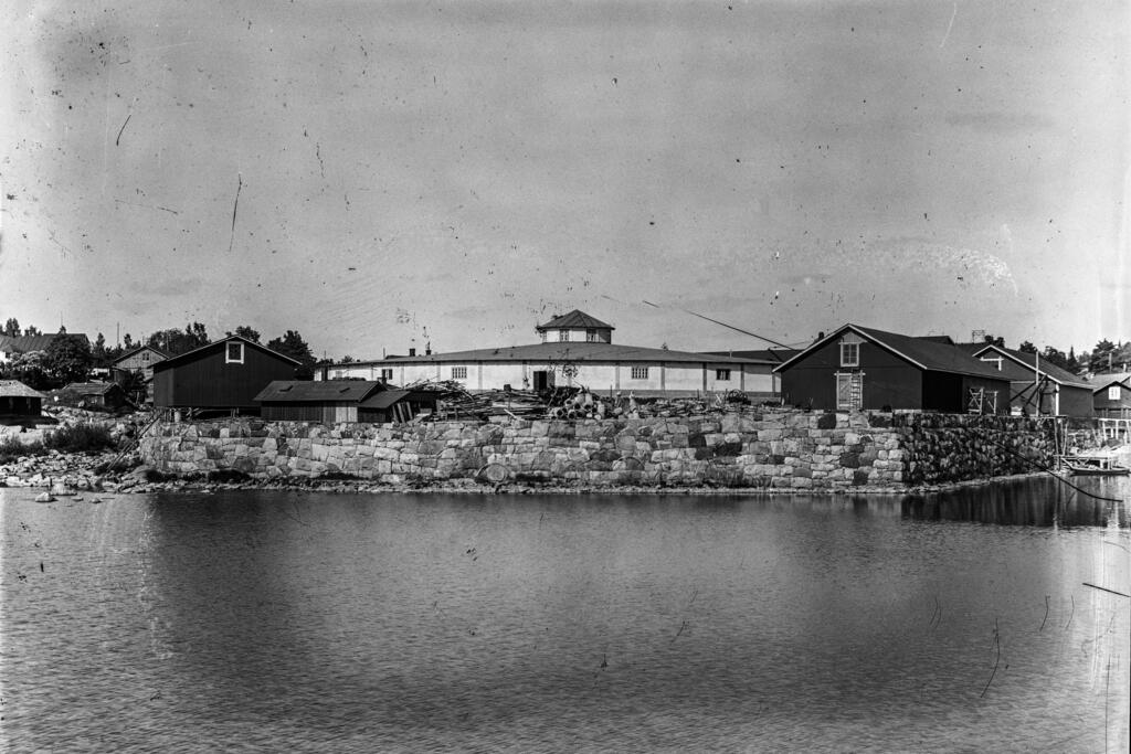 Kungsgårdsholmen i början av 1900-talet. På gården till den runda filterbyggnaden syns högar med rör och anslutningsstycken. Vattenledningsnätet utökades vid sekelskiftet med i genomsnitt ett par kilometer om året, så delar behövdes. Foto: Helsingfors stadsmuseum / Okänd fotograf