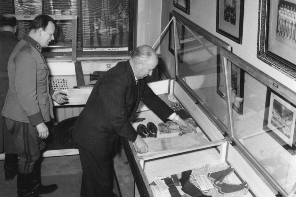 Kapteeni Väinö Virta (vas.) työskenteli museonhoitajana 1951–1965. Oikealla vuosien 1912 ja 1920 olympialaisten tähtijuoksija Hannes Kolehmainen on ottamassa vitriinistä vanhan kilpakumppaninsa Jean Bouinin paitaa.  Kuvaaja: TAHTO