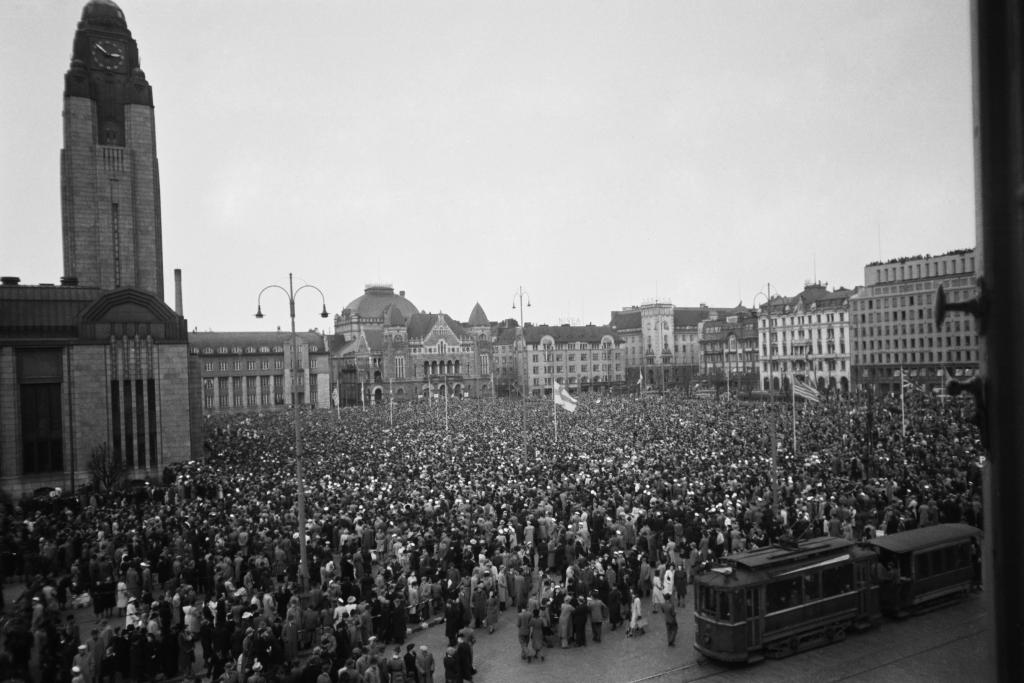 De allierades seger över Nazityskland firades på olika håll i Europa den 8 maj 1945, och även i Finland ordnades en fredsfest på Järnvägstorget på Kristi himmelsfärdsdag den 10 maj, där tusentals stadsbor deltog. I Ilta-Sanomat hade det dagen innan publicerats en annons där det utlovades ”uppsluppet hålligång med anledning av freden, swing och conga för ungdomarna, vals och polka för de äldre”. Fredsfesten ordnades av partierna på vänsterkanten, Agrarförbundet och Fredsförbundet.  Foto: Väinö Kannisto / Helsingfors stadsmuseum