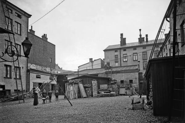 Aleksanterinkatu 52, sisäpiha. Sivuttain katsojaan seisoo nainen, jolla on lapsi sylissä. Kolme isompaa lasta seisoo rivissä keskellä pihaa. 