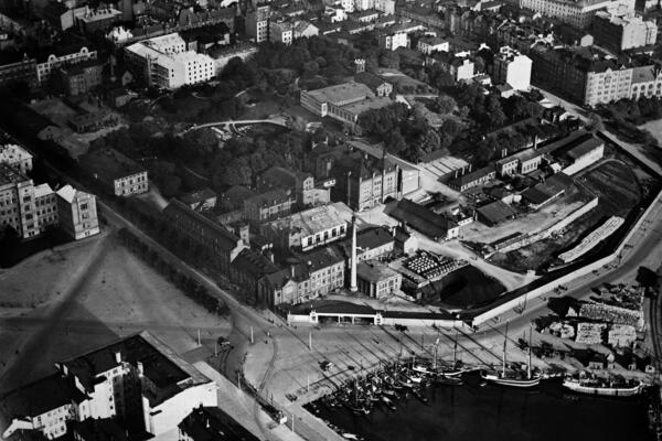 Flygbilden illustrerar Rödbergens och Sandvikens industriella historia. På bilden syns Sinebrychoffs fabriksområde med park, Bulevarden 40–42, Sandvikskajen 7, Maltgatan 1, Sandvikens bassäng och Sandvikens torg.