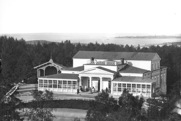 A white large building surrounded by a park. Many columns on the porch.