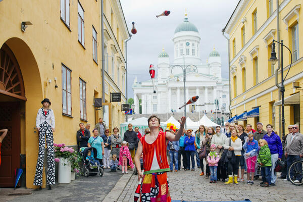 Etualalla jonglööri heittelee keiloja. Väkijoukko katselee taustalla, taka-alalla Tuomiokirkko.