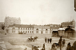 Hyrvagnar med sina hästar och herrskap vid Södra hamnen på Packhustorget. I bakgrunden det tidigare arméförrådet, från 1888 packhuset, Västra Hamngatan 10 (nuvarande Södra kajen 10). På gatan en hästdragen spårvagn. Bakom förrådet syns ett femvåningshus från 1960-talet vid hörnet av Unionsgatan 14 – Södra Magasinsgatan 3.